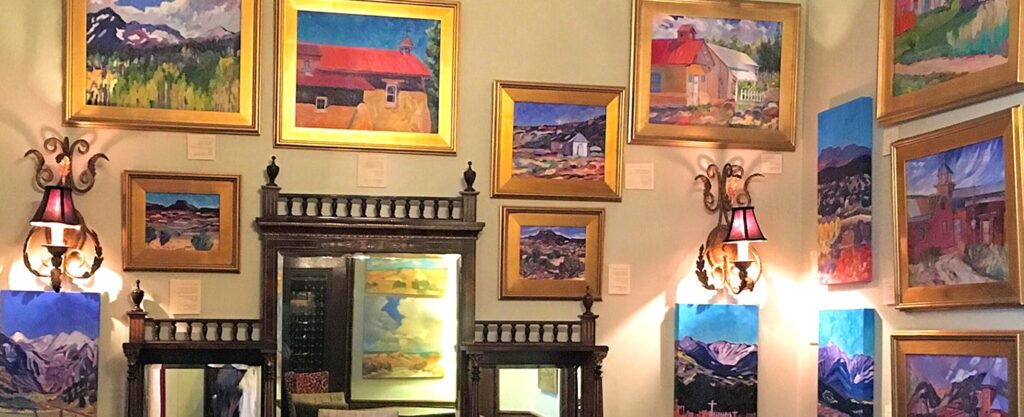 An interior room with paintings hanging salon-style on the walls, around a mirrored, dark, wooden sideboard.