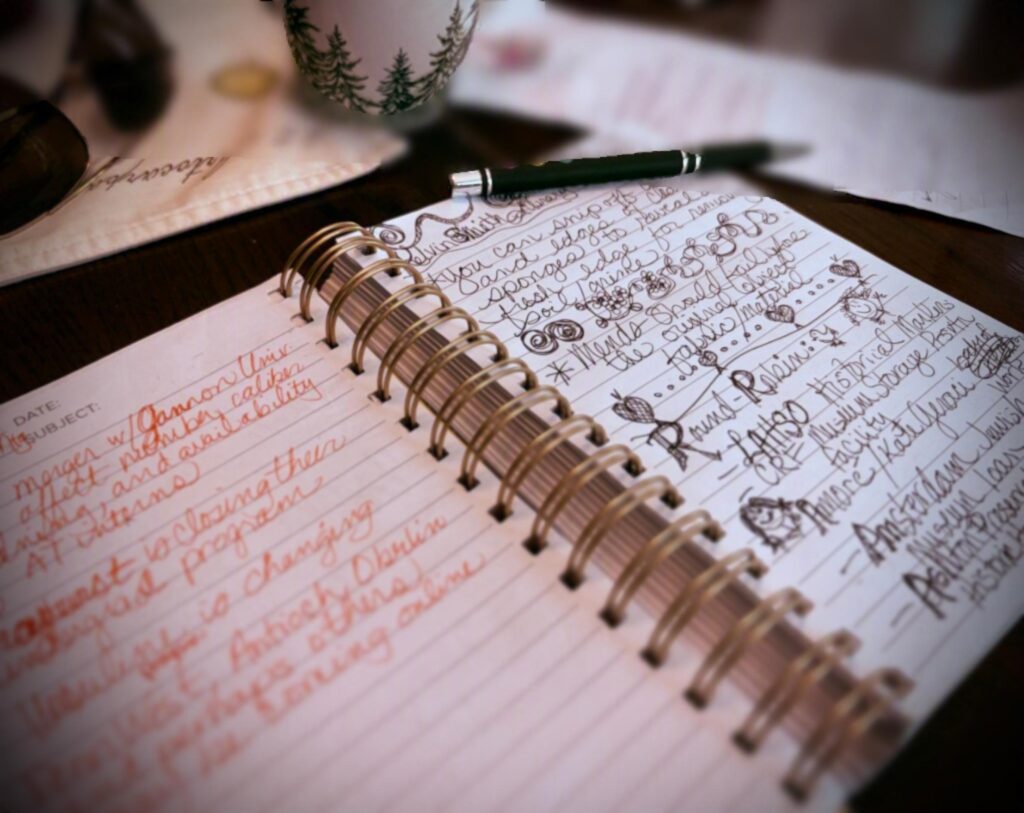 A blurry photo of a spiral-bound notebook filled with handwritten notes in orange and black ink, plus a bunch of messy doodles in the margins